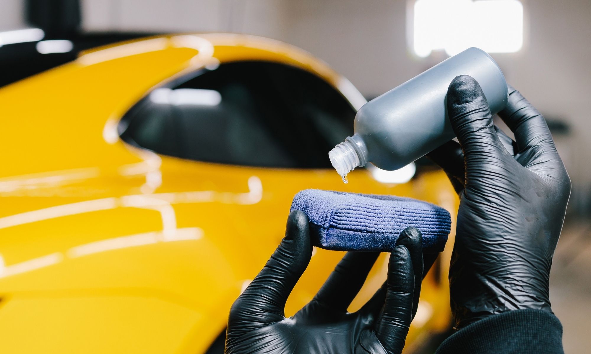 Gloved hands loading a ceramic coating applicator next to a yellow sports car
